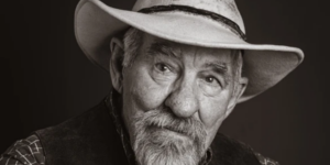 An old man with a cowboy hat and vest, radiating warmth and character in a classic Western style.