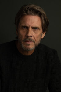 man sporting a beard and a black sweater, appearing deep in thought as he looks away.