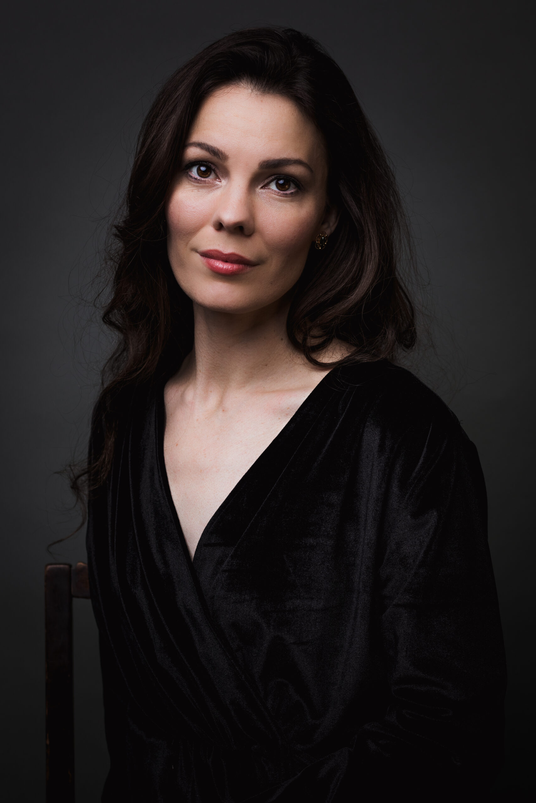 A woman in a black dress elegantly seated on a chair, exuding grace and poise in her posture.