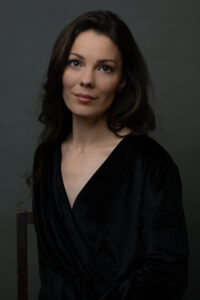 A woman in a stylish black dress is seated on a chair, embodying elegance and tranquility in her pose.