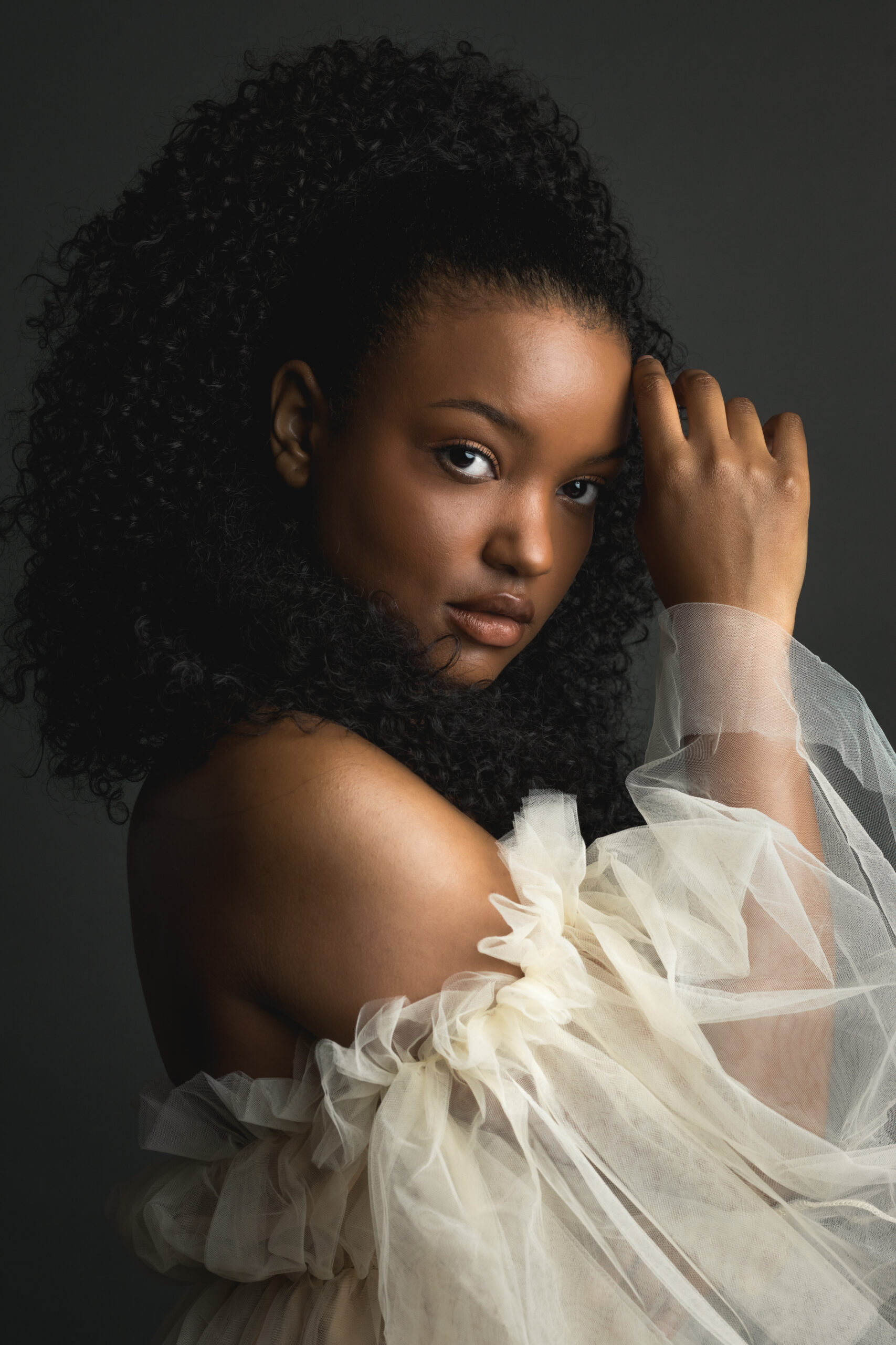 A stunning young woman with curly hair poses for a portrait.