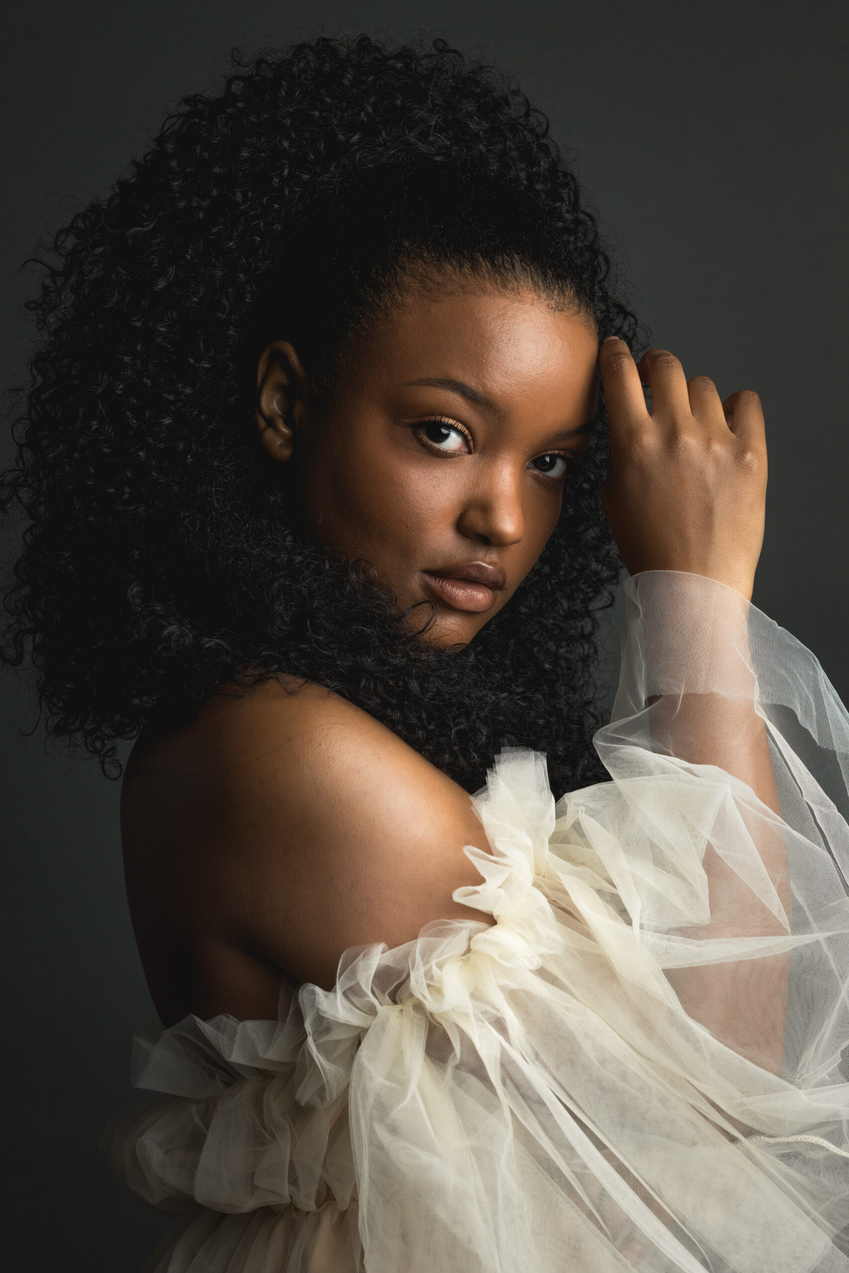 A beautiful young woman with curly hair poses gracefully for a portrait, showcasing her vibrant personality and charm.