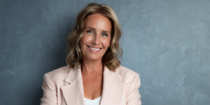 A woman wearing a pink blazer smiles warmly, radiating confidence and joy.