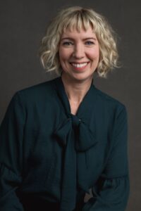 A professional corporate headshot of a woman with blonde hair wearing a bow tie, showcasing a confident business demeanor.