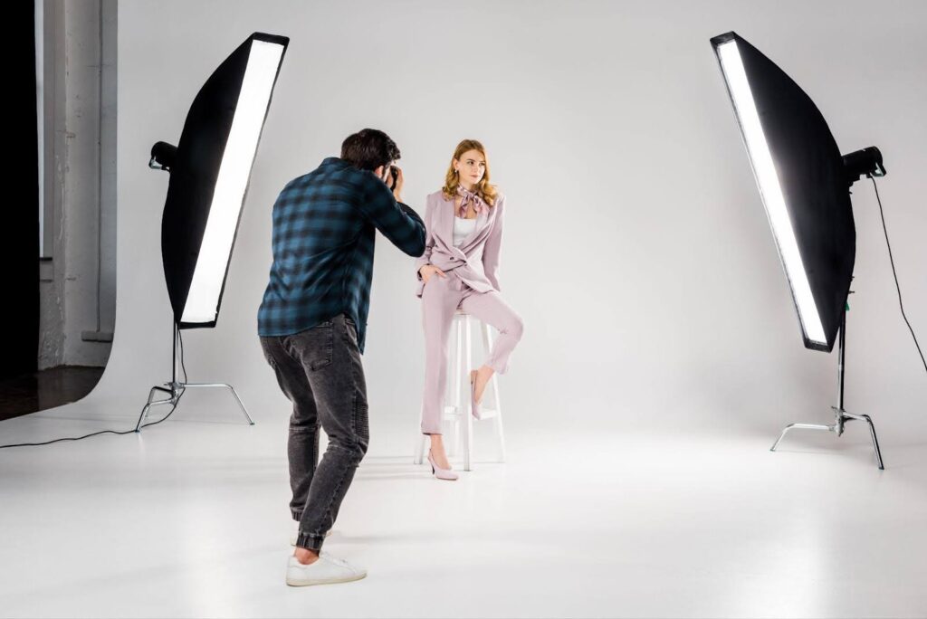 A man captures a photograph of a woman posing in a well-lit studio setting