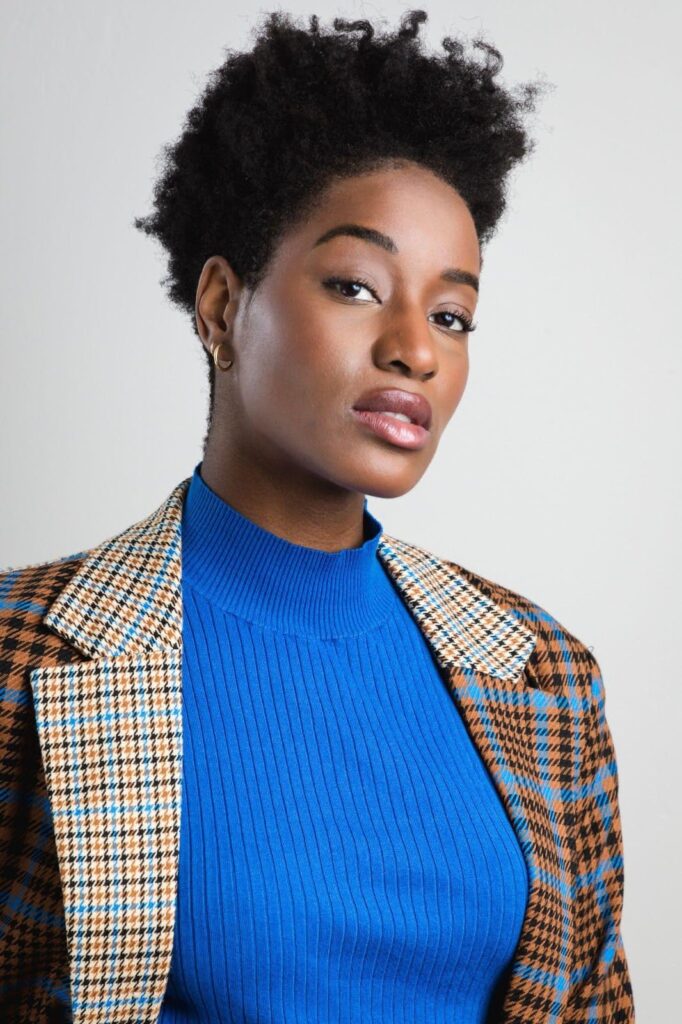 A short-haired woman in a blue sweater and plaid jacket exudes casual style