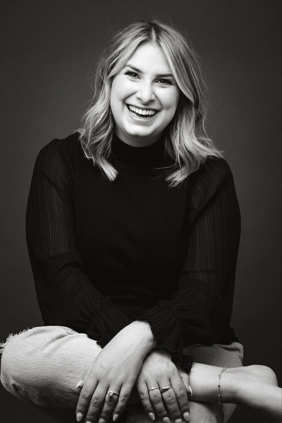 A woman sitting on a chair, smiling warmly, exuding joy and contentment in a relaxed setting