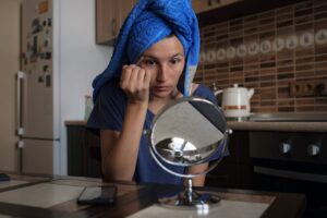 Woman applying makeup in front of a mirror at home, preparing for a professional appearance.