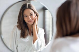 A woman smiles at her reflection in the mirror radiating joy and confidence